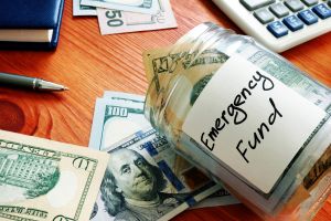 Glass jar labeled 'Emergency Fund' filled with cash, emphasizing the importance of setting aside a lump sum for financial security.